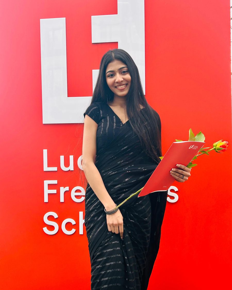 Ann Mariya im schwarzen Sari mit ihrer Abschlussmappe und einer Rose.
