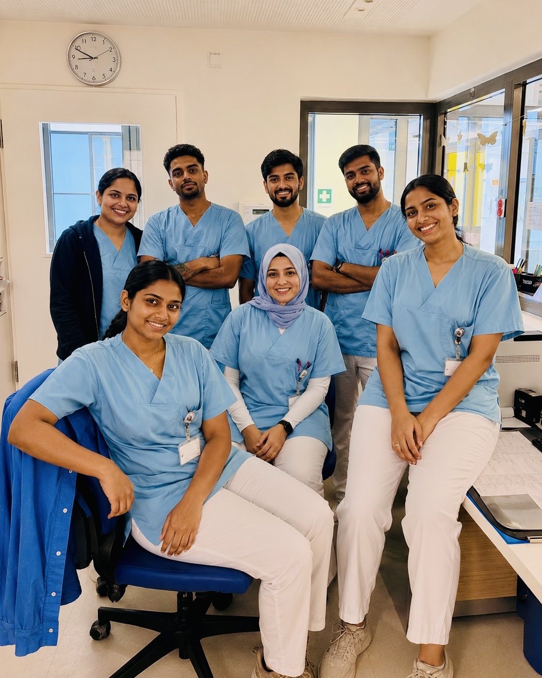 Ein Pflegeteam in blauer Dienstkleidung im Stationszimmer einer Klinik.
